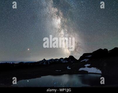 Bellissimo scatto di montagna innevata vicino a uno stagno sotto a. cielo pieno di stelle Foto Stock