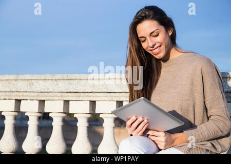 Donna sorridente con il suo tablet mentre è seduto su una panchina di pietra Foto Stock