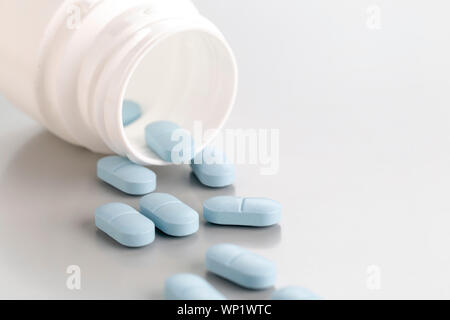 Un close-up di una pastiglia in bottiglia con un paio di blu pillole di antibiotico. Vista frontale, sfondo grigio chiaro Foto Stock