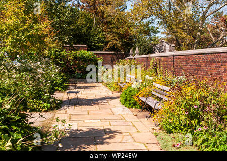 Una passerella di pietra in un giardino di fiori con due panche di legno e un muro di mattoni in estate di Pittsburgh, in Pennsylvania, STATI UNITI D'AMERICA Foto Stock