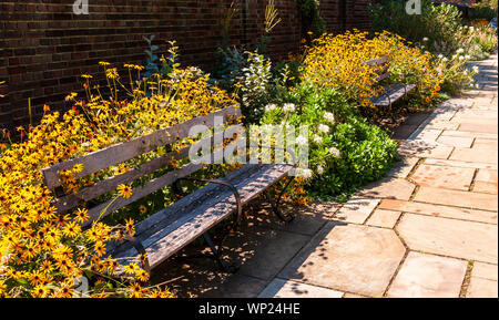 Una passerella di pietra in un giardino di fiori con due panche di legno e un muro di mattoni in estate di Pittsburgh, in Pennsylvania, STATI UNITI D'AMERICA Foto Stock