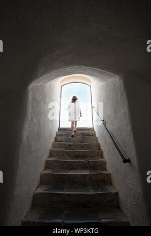 Giovane donna a piedi fino a tall ripida rampa di scale verso l'uscita e la luce del sole in alto in un vecchio edificio visto dal basso delle fasi Foto Stock