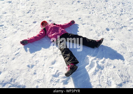 Bambina facendo una snowangel indossando vestiti di neve Foto Stock