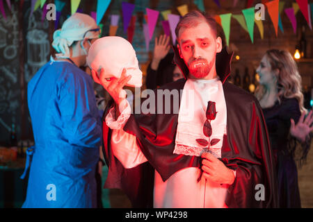 Il conte Dracula tenendo un teschio umano e guardando nella telecamera alla festa di Halloween. Scary espressione. Foto Stock