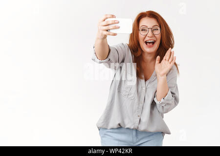 Felice allegro carino redhead di mezza età granny dicendo ciao nipoti parlando videocall famiglia smartphone attesa grin hi sventolando saluto guardare telefono Foto Stock