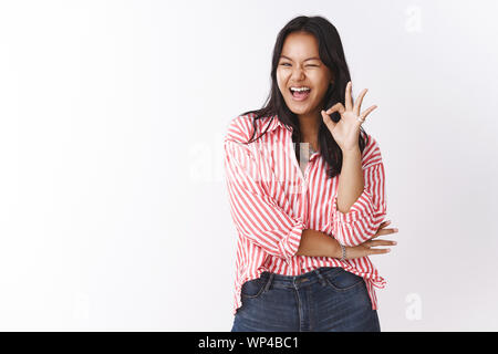 Wow awesome andate ragazza. Ritratto di divertito e impressionato upbeat bella elegante donna asiatica in camicia a righe con una strizzatina d'occhio sfrontato e mostrando buone condizioni si Foto Stock