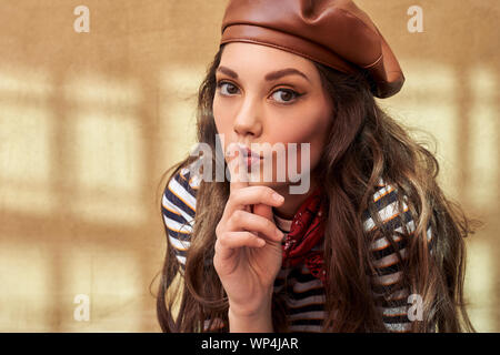 Giovane bella bruna ragazza vestita rétro in stile vintage nella vecchia città europea fa un gesto hush Foto Stock