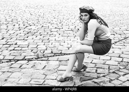 Giovane bella bruna emotional ragazza vestita rétro in stile vintage nella vecchia città europea si siede in una catena Foto Stock