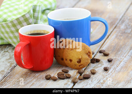 Colorato due tazze di caffè nero su rustiche superficie in legno con biscotti e caffè in grani sparsi intorno Foto Stock