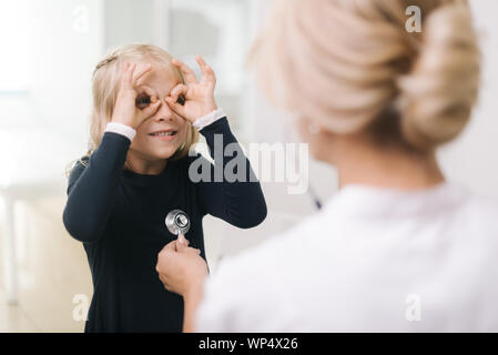 Funny Girl ingannare circa quando il pediatra con uno stetoscopio sta esaminando la sua Foto Stock