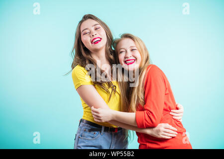 Felice brightful momenti positivi di due ragazze eleganti avvolgente su sfondo blu. Closeup ritratto divertente gioiosa attarctive giovani donne divertendosi, smi Foto Stock