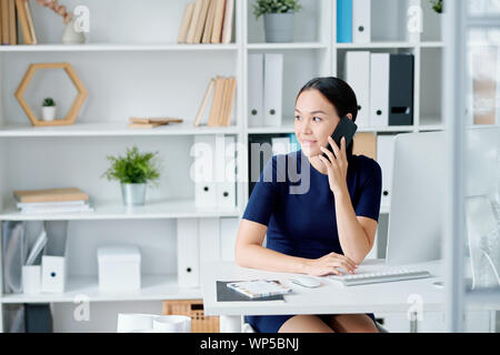 Piuttosto giovane imprenditrice bruna con lo smartphone i client di chiamata Foto Stock