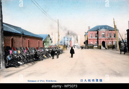 [ 1910s Giappone - Yokohama Pier ingresso ] - una lunga fila di risciò all'ingresso del molo nel porto di Yokohama, nella prefettura di Kanagawa. L'edificio di mattoni rossi a destra è il porto di Kanagawa Office (神奈川県港務部). È stato progettato da architetto inglese Josiah Conder (1852-1920). Per accogliere navi di grandi dimensioni, la costruzione di un molo di ferro è stato iniziato nel 1889 (Meiji 22) e completata nel 1894 (Meiji 27). È stato progettato da esercito britannico ingegnere Henry Spencer Palmer (1838-1893), e costruito da Zentaro Mita (三田善太郎, 1855-??). Xx secolo cartolina vintage. Foto Stock