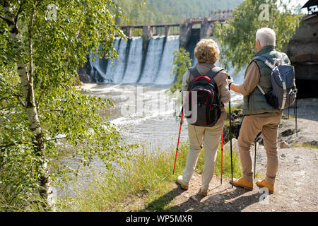 Vista posteriore della coppia matura con zaini in piedi sulla riva del fiume Foto Stock