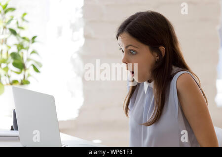 Scioccato giovane donna leggere notizie incredibili su laptop Foto Stock