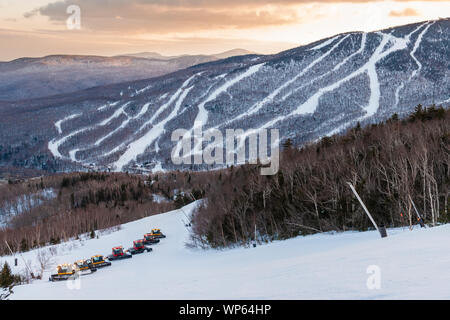 Una flotta di gatti battipista toelettatura Spruce Peak al tramonto con il Mt. Mansfield in background, Stowe Vermont, USA Foto Stock