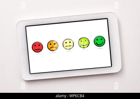 Soddisfazione dei livelli di rappresentazione con le emoticon su bianco tablet schermo sul tavolo bianco vicino. Composizione orizzontale. Vista dall'alto. Foto Stock