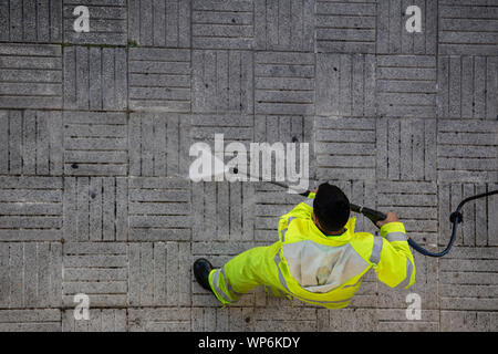 Vista dall'alto di un lavoratore la pulizia del marciapiede di strada con il getto di acqua ad alta pressione. Pubblica il concetto di manutenzione Foto Stock
