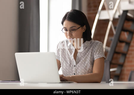 Grave focalizzata asiatica dei dipendenti di sesso femminile in bicchieri a lavorare con il computer. Foto Stock