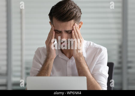 Colpo alla testa infelice giovane maschio dipendente che soffre di un forte mal di testa. Foto Stock