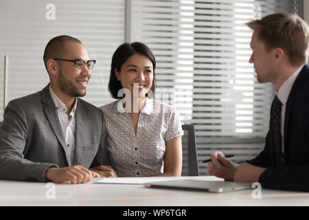 Sorridente razza mista famiglia giovane incontro agente immobiliare. Foto Stock