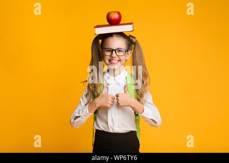 Schoolgirl gesticolando Thumbs-Up azienda prenota e Apple sulla testa Foto Stock