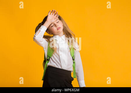 Little Schoolgirl Sensazione di cattivo di toccare la testa, sfondo giallo Foto Stock