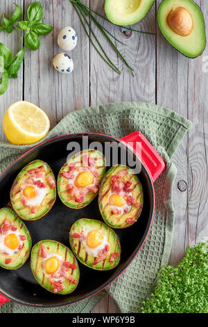 Vista dall'alto su grigliate di barche di avocado con pancetta e uova di quaglia, piatto giaceva su sfondo di legno Foto Stock