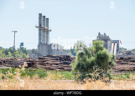 Un grande mulino di legname nel sud della Oregon con tre grandi pile di fumo e plles di tronchi di alberi pronti per l'elaborazione in primo piano. Foto Stock