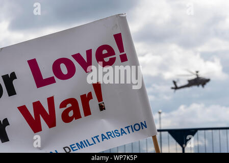 US Army AH-64 Apache gunship in atterraggio a difesa della sicurezza & Equipment International DSEI arms fair trade show, Excel, London, Regno Unito. Banner di protesta Foto Stock