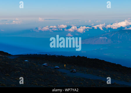 Vetture scendendo la strada dal cratere Haleakala dopo la visione di un colorato sunrise, Maui, Hawaii, STATI UNITI D'AMERICA Foto Stock