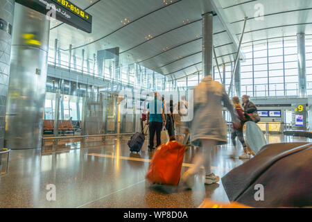 DOHA IN QATAR - Luglio 13 2019; i passeggeri in attesa in linea con il bagaglio pronto a salire a bordo del piano come peopson con sacchetto rosso passa dietro sfocato in motion illus Foto Stock