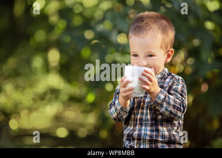 Little Boy bere yogurt o latte dal vetro esterno Foto Stock