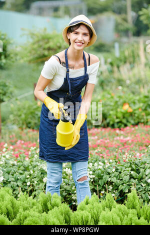 Piuttosto sorridente specialista di giardinaggio di spruzzatura di piante in vivaio per proteggerli dalla malattia fungina Foto Stock