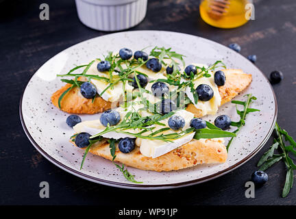 La bruschetta. Tostare i crostini con frutti di bosco freschi mirtillo e miele, formaggio brie, rucola. Cucina italiana Foto Stock