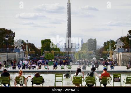 Persone sedute in sedie verde intorno al bacino ottagonale all'estremità occidentale dei Giardini Tuileries, l'obelisco egizio nel posteriore, Paris, Francia. Foto Stock