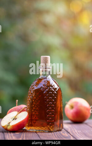 Sidro di mele o aceto in vetro decanter e mature mele fresche sul tavolo in legno all'esterno Foto Stock