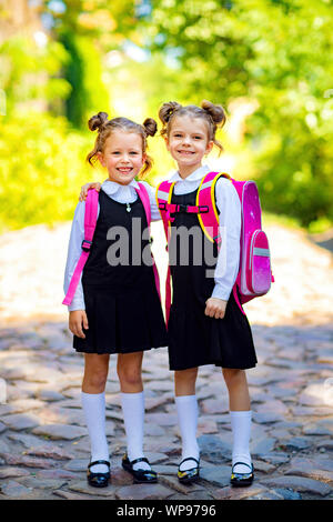 Due studenti sorridente ragazza che indossa la scuola zaino. Ritratto di felice Caucasian giovane ragazza al di fuori della scuola primaria. Sorridente schoolgirl guardando la fotocamera. Foto Stock