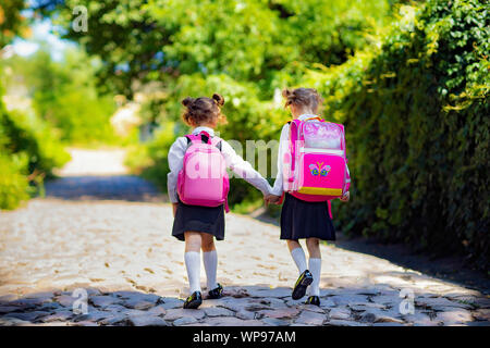 Vista posteriore di una scuola di due ragazze che indossano uno zaino al di fuori della scuola primaria. schoolgirl, scuola elementare studente andando a scuola, graduazione vacanze estive. Foto Stock