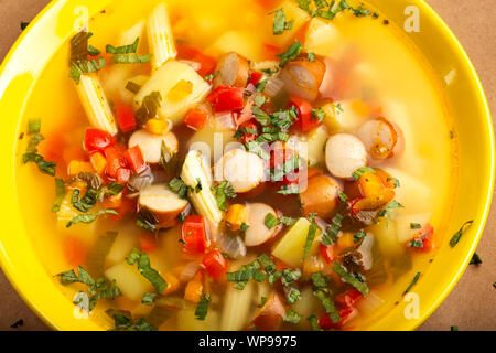 Minestra di verdura, di salsicce e di pasta in una piastra di colore giallo - vista superiore Foto Stock