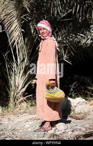 Giovane uomo in abiti tradizionali che indossa foulard di testa e tenendo un cestello, Oman Foto Stock