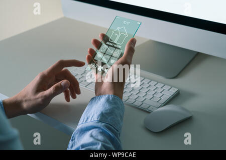 Un uomo utilizza un avveniristico telefono trasparente con applicazione per il controllo smart house. Foto Stock