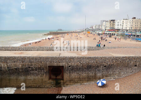 Sun solitaria adoratore siede sotto il loro ombrellone da un emissario groyne tubazione sulla famosa Spiaggia di Brighton. Foto Stock