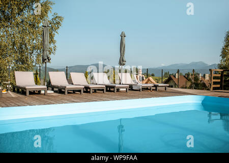 Bella piscina con lettini per prendere il sole in montagna, donna rilassante sullo sfondo Foto Stock