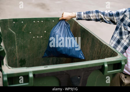 Maschio rifiuti di dumping il pacchetto in un grande cestino di contenitori Foto Stock