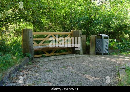 Legno sedile unico con pali in pietra bidone dei rifiuti sentiero di ghiaia di alberi e arbusti in Honley Huddersfield nello Yorkshire Inghilterra Foto Stock