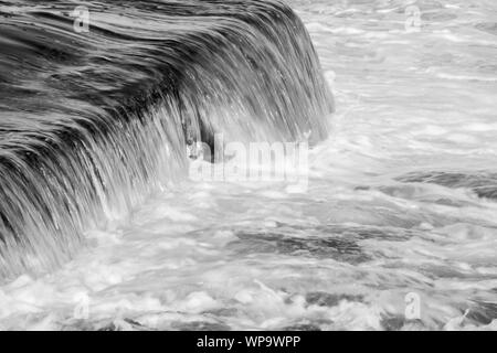 In bianco e nero fotografie astratte di un paesaggio marino con forte risacca con acqua che scorre su un pool di marea parete in corrispondenza di un otturatore a bassa velocità - potente Foto Stock