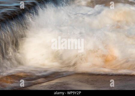 Pomeriggio Un forte, marea. Le onde sono di schiantarsi su una marea di parete della piscina e creando un potente flusso di ritorno. Surf schiumoso e potenti flussi di crash Foto Stock