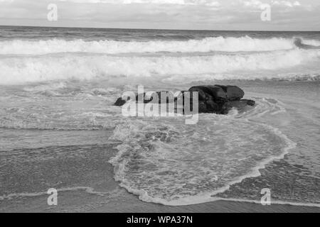 Un bel bianco e nero seascape con serena e spumeggianti acque. Le onde si infrangono contro una roccia nel tardo pomeriggio. Foto Stock