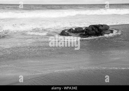 Un bel bianco e nero seascape con serena e spumeggianti acque. Le onde si infrangono contro una roccia nel tardo pomeriggio. Foto Stock